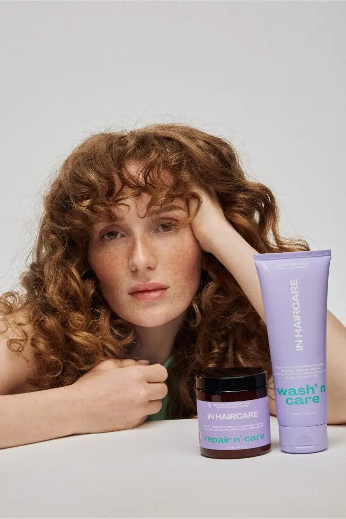 Modèle aux cheveux bouclés présentant les soins capillaires IN Haircare Repair N Care masque et Wash N Care shampoing